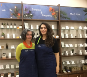 Οι ιδρύτριες της FISIKA, μητέρα και κόρη, Φυλιώ και Μαρία Συκά στέκονται μπροστά στα ράφια του καταστήματός τους που είναι γεμάτα με τα προϊόντα τους