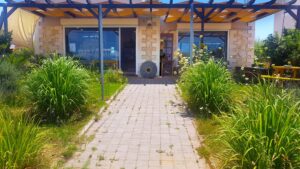 Το εργοστάσιο και κατάστημα FISIKA με πέτρινη πρόσοψη και έναν βοτανικό κήπο μπροστά.